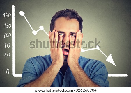 Portrait frustrated stressed young man desperate with financial market chart graphic going down on grey office wall background. Poor economy financial crisis concept. 