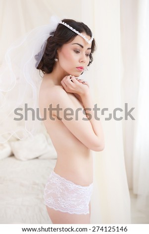 Beautiful topless bride with a beautiful figure standing by the bed, and about something thinks. Bride getting ready on her wedding day