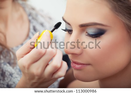 Make-up artist applying mascara on model\'s eyelashes, close-up, selective focus on lashes and brush
