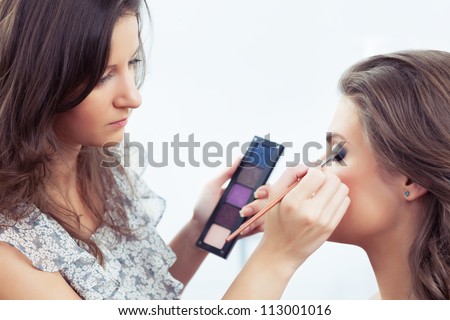 Make-up artist holding eye shadow palette and applying make-up, selective focus on model\'s eye