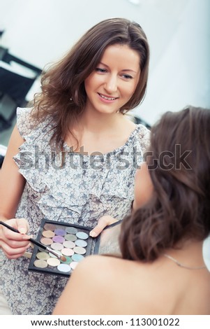 Make-up artist at work holding eye shadow palette and brush, choosing color, looking at model