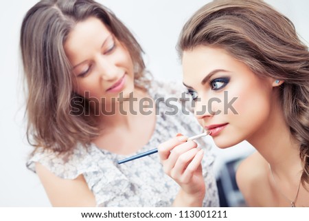 Make-up artist applying lipstick with a brush on model\'s lips, close-up