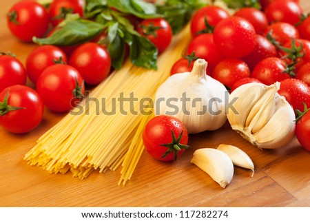 Pasta, tomatoes, garlic and basil on wooden table, focus on foreground