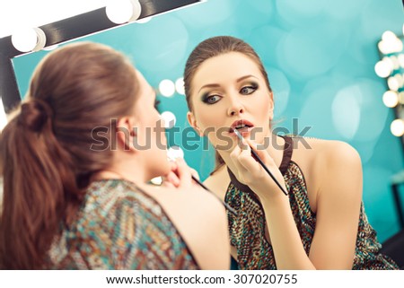 Young woman applying lipstick with a brush in front of a mirror