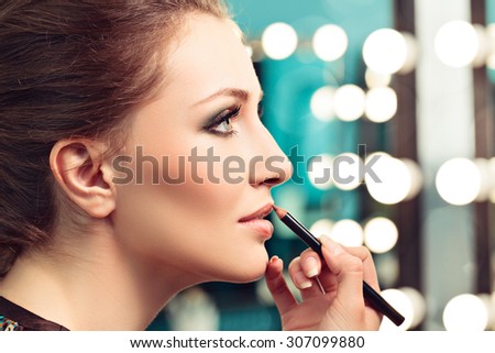 Make-up artist applying lip liner on model\'s lips, focus on model\'s eye