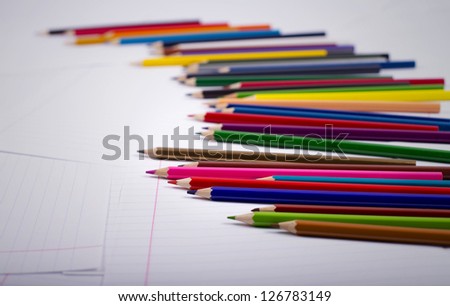 color pencils are randomly scattered on a surface from writing-book sheets