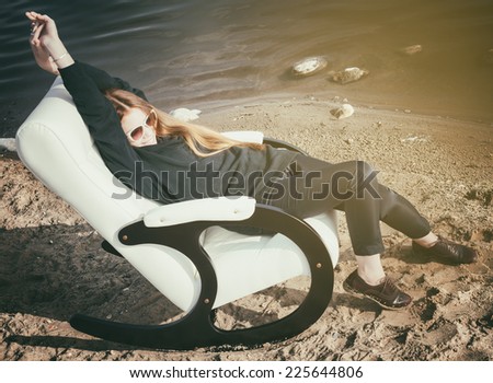 beautiful happy woman has a rest in chair on bank of the lake morning