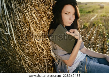beautiful girl hipster reads book against hay bale in fall