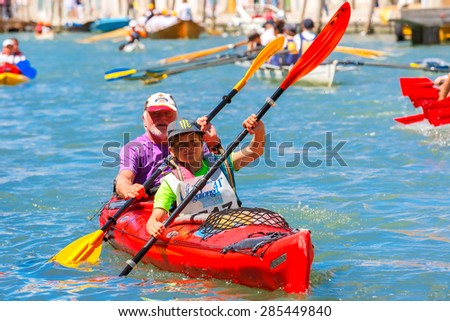 Venice, Veneto, Italy - May 24, 2015: Boy and man oarsmen, in red boat race along the Cannaregio Canal in the Venice Vogalonga regatta. More than 1,500 boats take part in the annual historic regatta