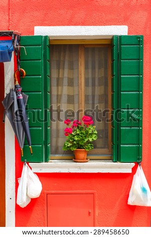Picturesque window with green shutters and flowers on red wall of houses on the famous island Burano, Venice, Italy