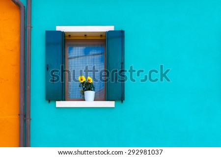 Picturesque windows with shutters and flowers on blue and orange wall of houses on the famous island Burano, Venice, Italy