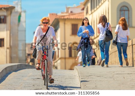 Florence, Italy - May 19, 2015: Caucasian woman cyclist on the Bridge of Santa Trinita over river Arno, Tuscany.