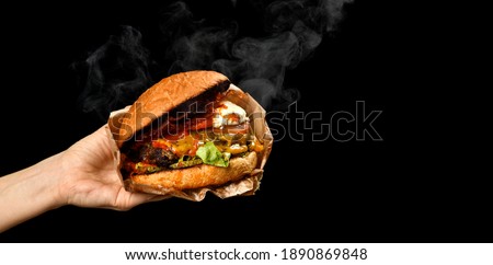 Hands hold big Burger cheeseburger sandwich with marble beef lettuce tomato cheese bacon with steam smoke on black background