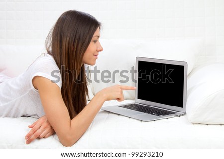 Young successful woman lying on a sofa with laptop paying bills online looking up and thinking