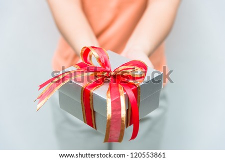 hand give silver gift box with red and gold ribbon