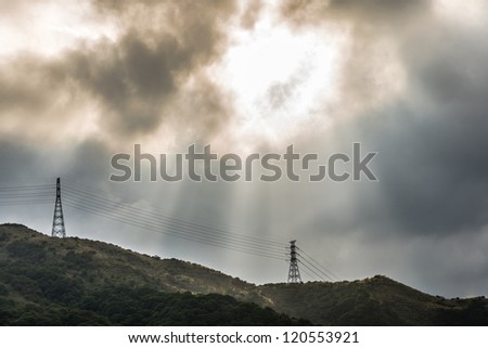 sun light beam through rain cloud over high voltage electrical wire and mountain
