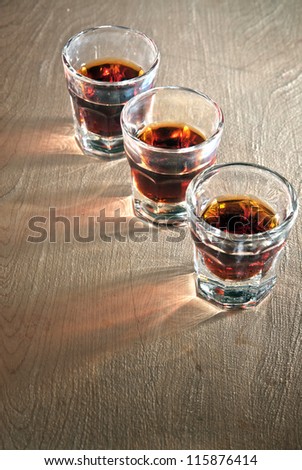 Three shot glasses full of dark colored alcohol on top of a bar table.