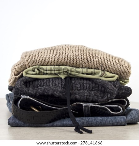 Stack of clothes on a Wooden table  in front of the white wall.