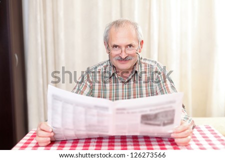 Elderly man reading the newspaper at home.