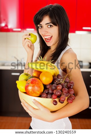 Healthy young woman biting an apple and holding a dish full of fruits.