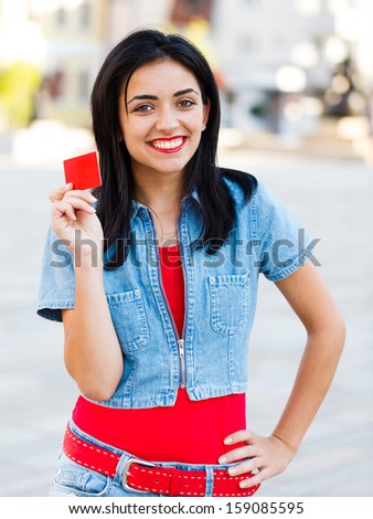 Smiling brunette woman holding a red empty credit card in the city center.