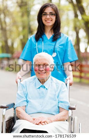 Nice nurse walking with elderly lady in wheelchair.