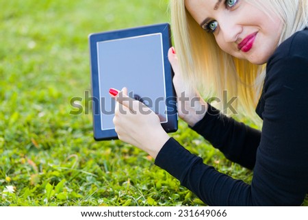 Pretty girl showing tablet on grass.