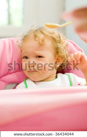 A cute little baby fed by her mother with a spoon, with a sad facial expression, she does not want to eat.