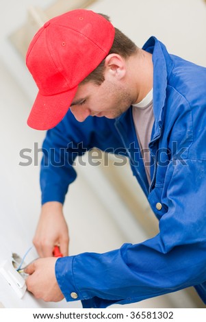 A young electrician installing an electrical switch / plug in a new house.