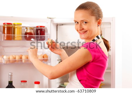 A young woman using the refrigerator, reaching for eggs. Food, milk, red wine and juice in the background.