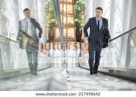 Businessman smiling with his own reflection at the escalator