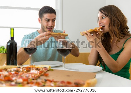 People biting a slice of pizza pie supreme style with drinks and having fun