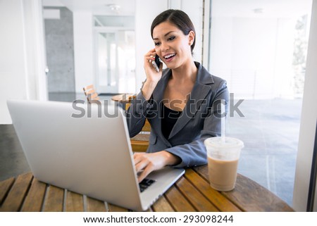 Beautiful Business woman at a coffee shop working on a laptop and talking on the cell phone