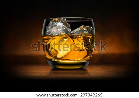 Single glass of whisky whiskey bourbon on ice on top of a wood bar table and wooden background