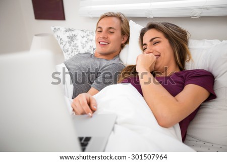 Couple in bed watching movies on computer laptop streaming video clips entertainment tv