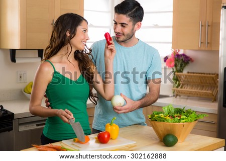 Lovers couple cooking vegetables and preparing an organic salad in the kitchen playful fun funny