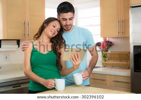 Couple man and woman sharing smart tablet with coffee at home hugging intimate loving video streaming