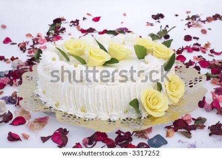 big white creamy cake with yellow roses and petals spread on white backgroung