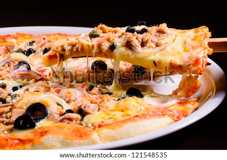 Pizza lifted slice with tuna isolated over black  background