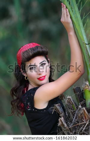 Beautiful young woman with pin-up make-up and hairstyle posing near a tree