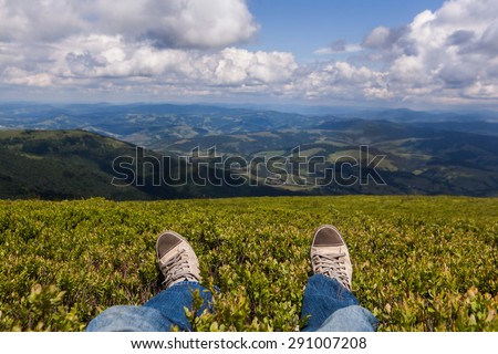 Man sitting on a high mountain top with first person perspective view, legs in focus