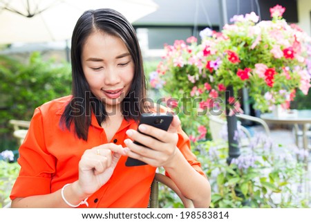 Young woman using smartphone in a sidewalk cafe restaurant with beautiful garden