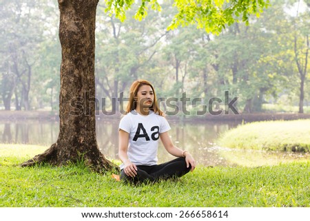 Young asian woman doing yoga in the Lotus position at the green natural park