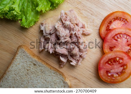 Canned tuna meat prepared for sandwich with bread, lettuce and tomato on wood background