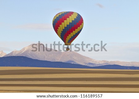 Colorful Hot air balloon with the stripes of agriculture farmlands in the foreground and the Twin Peaks, Mt Meeker 13,911 feet and Longs Peak 14,256 feet.
