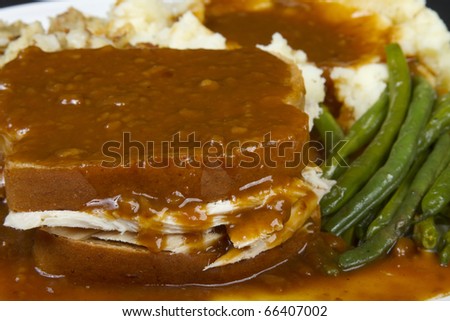 Thanksgiving holiday leftovers. Close-up of a hot Turkey sandwich smothered in gravy with mash potatoes and green beans.