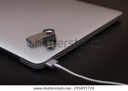 Silver charging laptop with flash usb disk on key. Soft focus, put on disk on key usb connector.