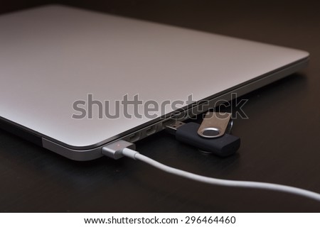 Silver charging laptop with flash usb disk on key. Soft focus, put on disk on key usb connector.