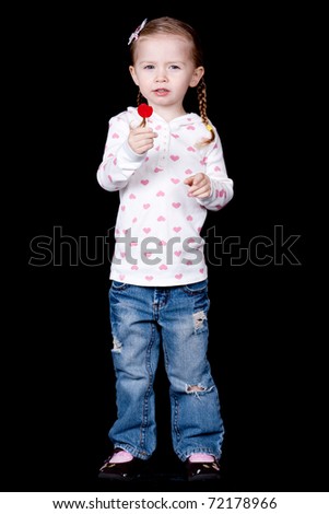 A full body shot of a young girl holding a lolly pop.  There is a black background.