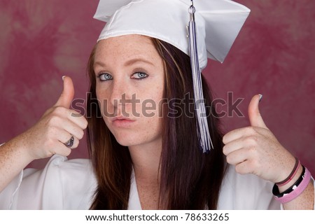 A cute girl poses for her graduation photo.  There is a pink background.